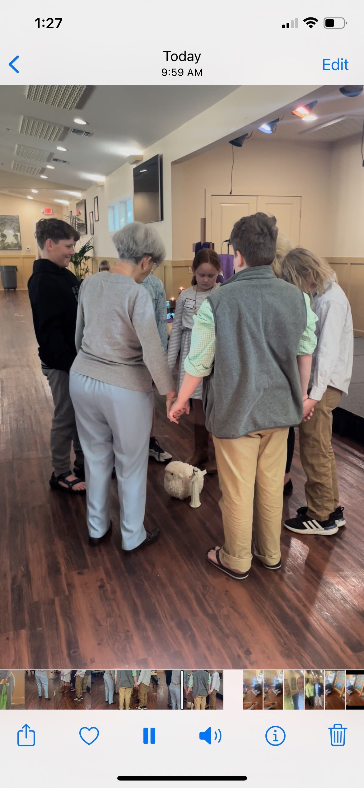 People holding hands in a circle, with a small dog inside, in a room with wood floors.