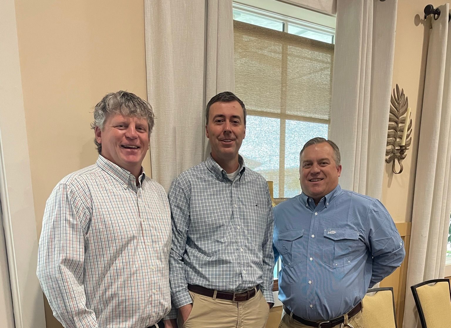 Three men in button-down shirts stand in church, smiling. 