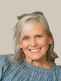 Woman with blonde hair, smiling, wearing a blue shirt and small hoop earrings. Sunglasses on head.