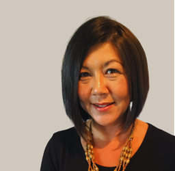 Woman with short dark hair smiling, wearing a black shirt and gold necklace.