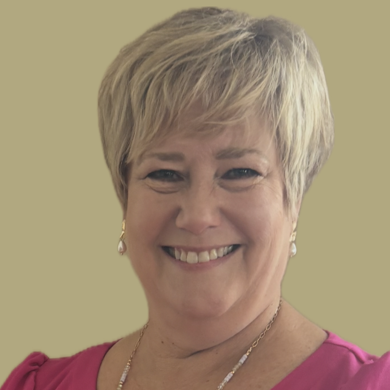 Woman with short blonde hair smiles, wearing a pink top and pearl earrings, against a tan background.