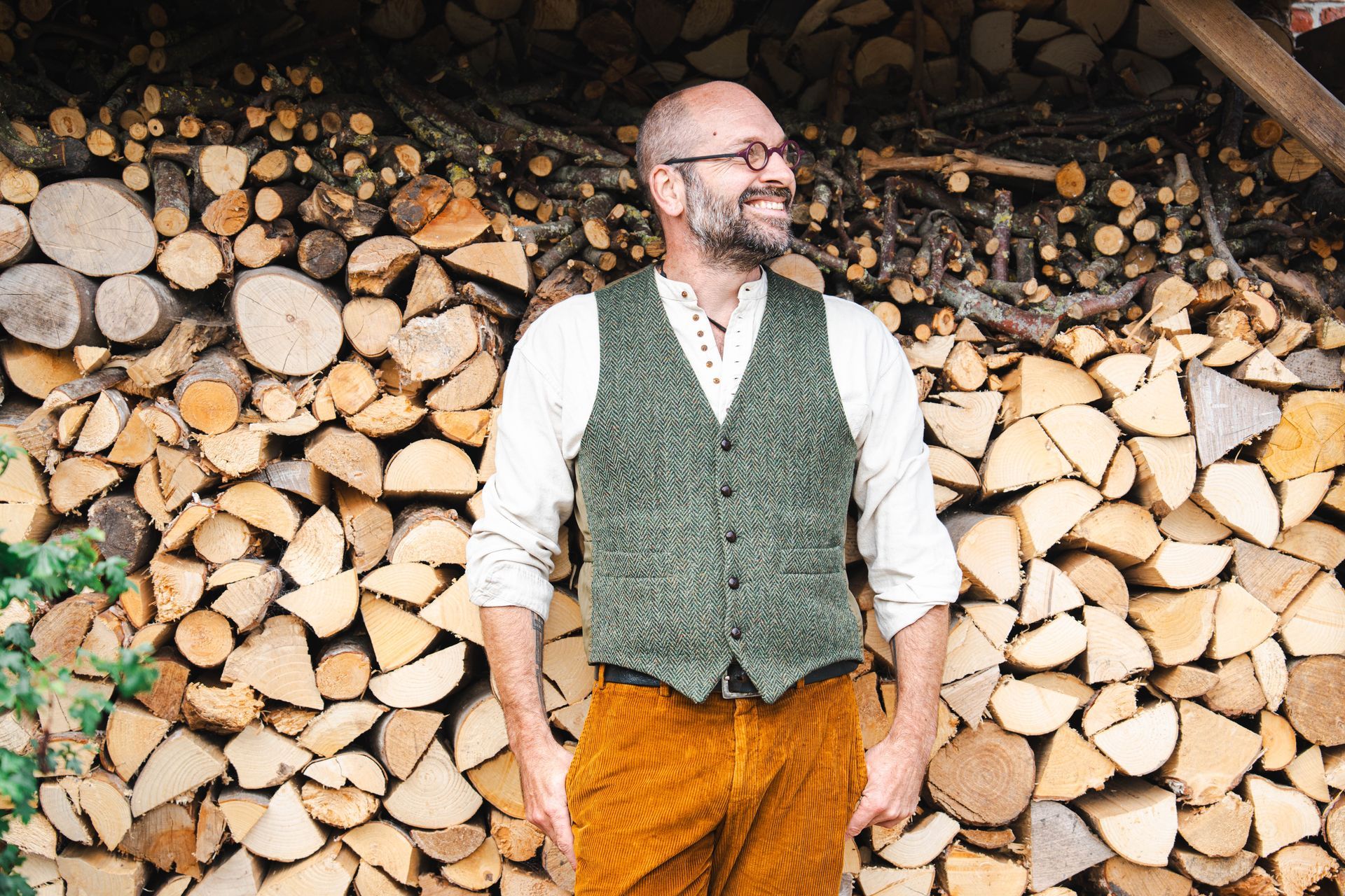 Bas van der Tang en een vest staat glimlachend voor een stapel brandhout.