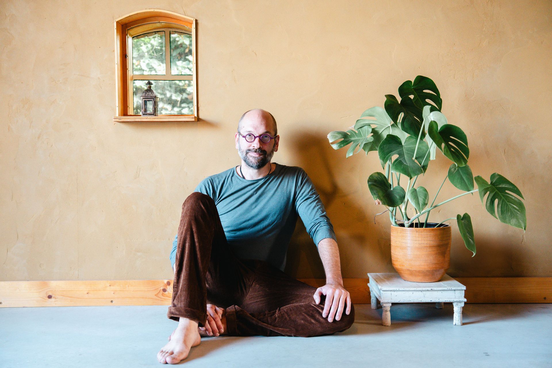 Bas zit op de grond, leunend tegen een beige muur, naast een potplant.