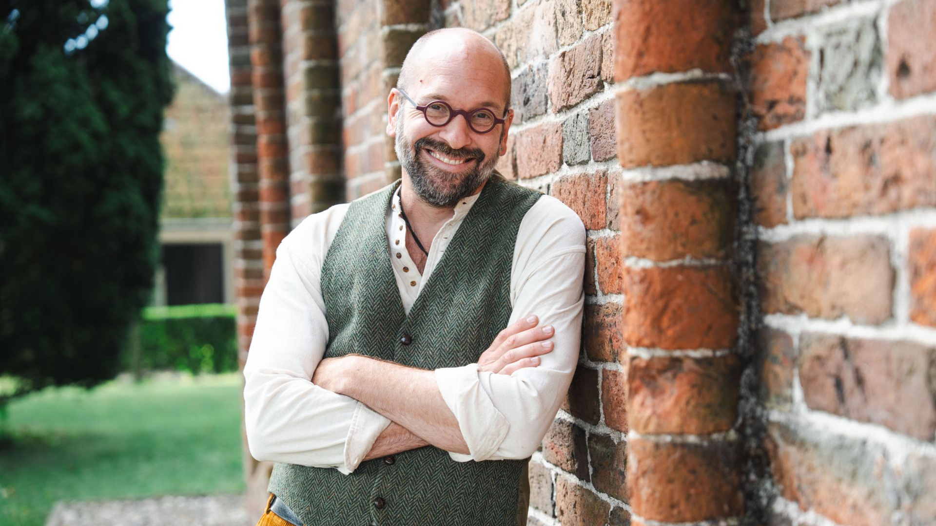 Bas leunt tegen een bakstenen pilaar. Buiten.