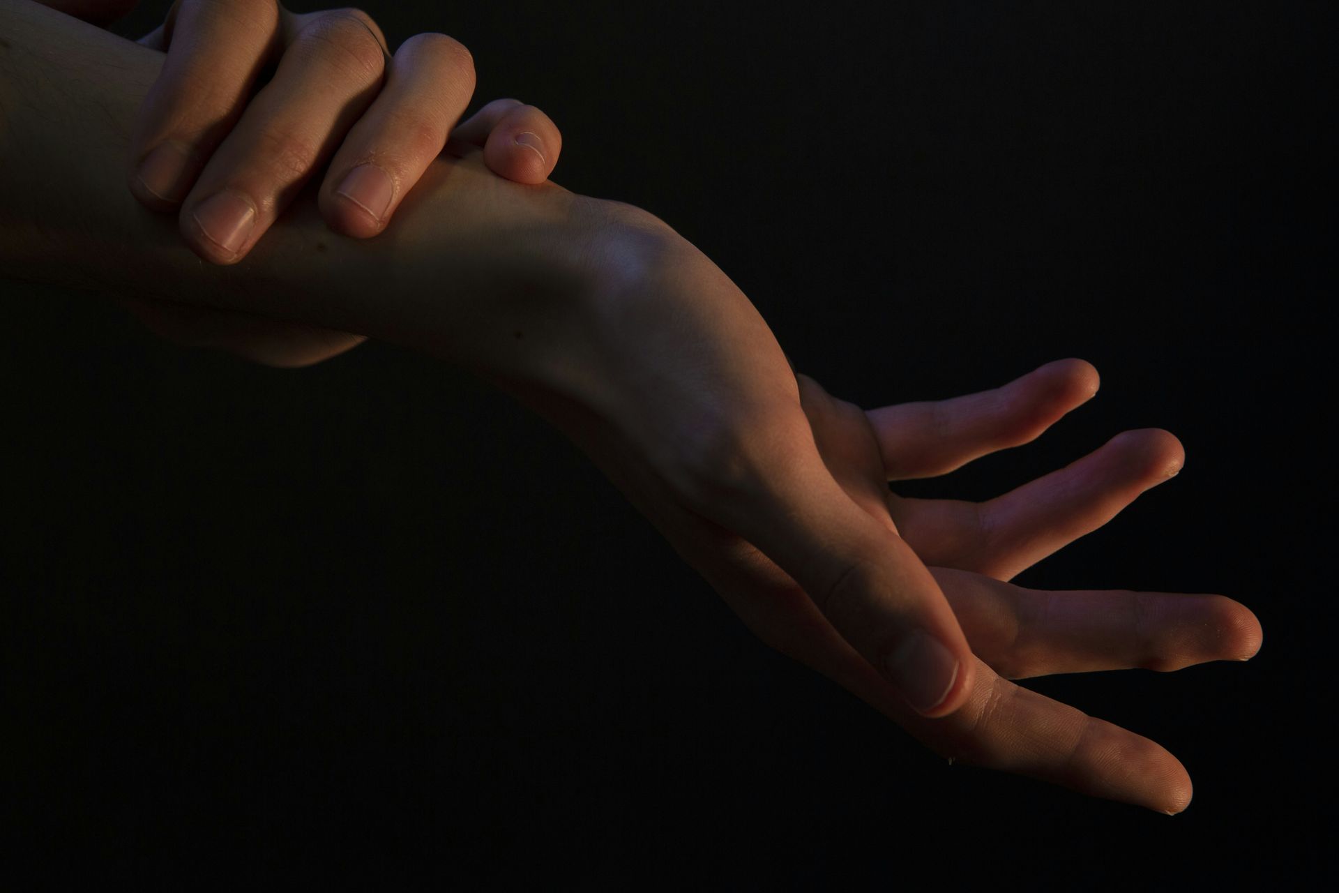 Arm and hand reaching, illuminated against a dark background, fingers extended.