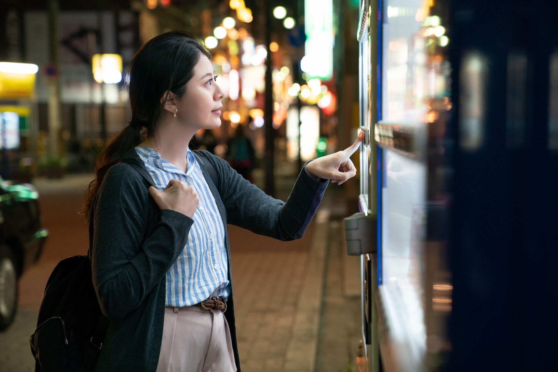 A woman is using a vending machine at night.