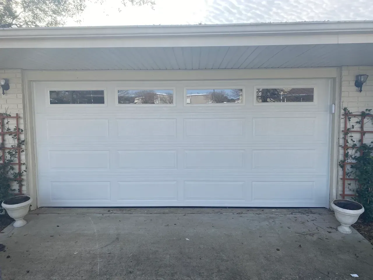 White garage door with rectangular windows above, flanked by potted plants.