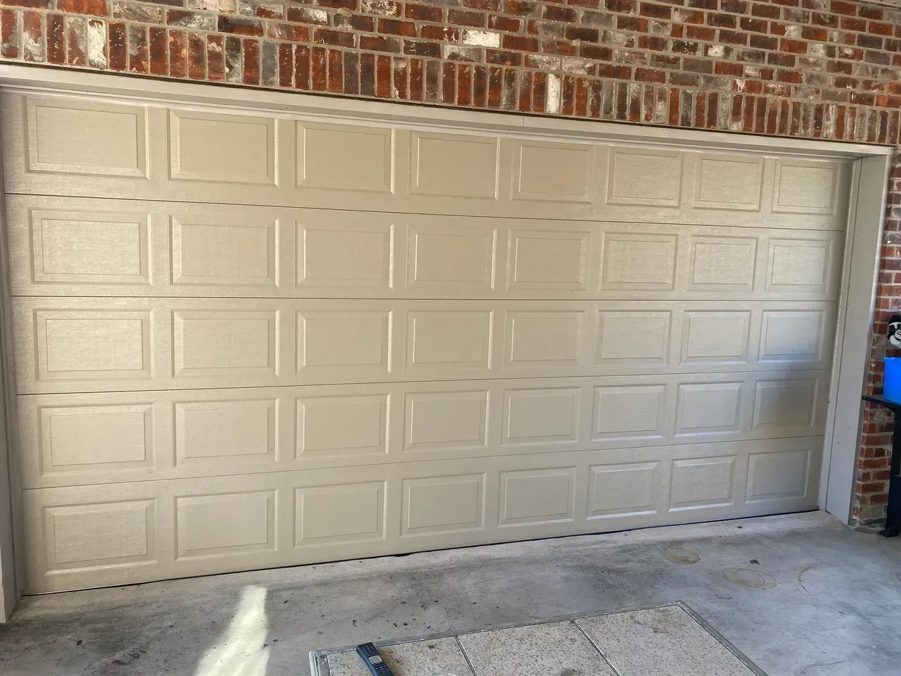 Tan garage door with square panel design, under brick facade and white trim.