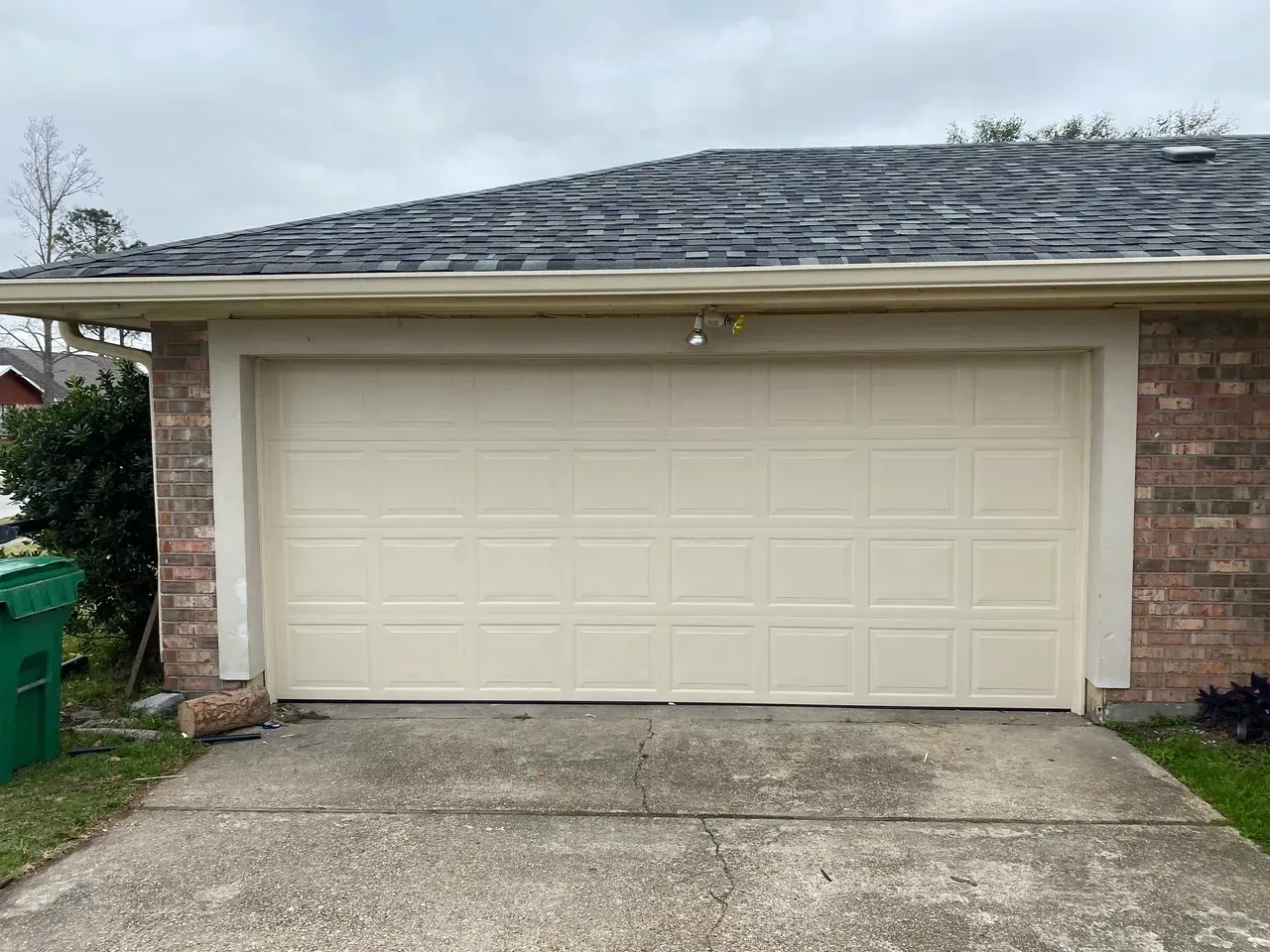 Cream-colored garage door on a brick building with a concrete driveway and gray roof.