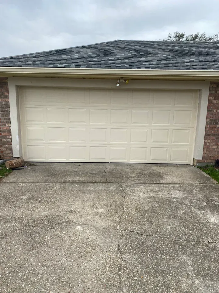 Garage with a closed cream-colored door on a concrete driveway in front of a brick house.