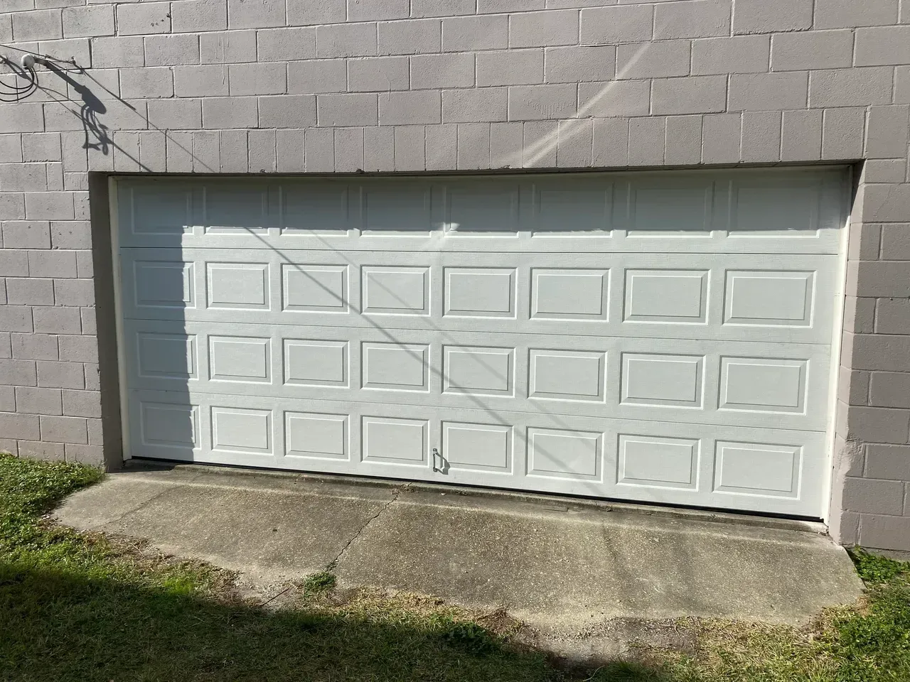 White garage door on gray brick wall, angled concrete base, sunny day.