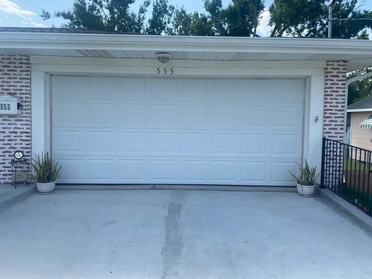 White garage door with brick accents. Plants flank the garage. Concrete driveway.