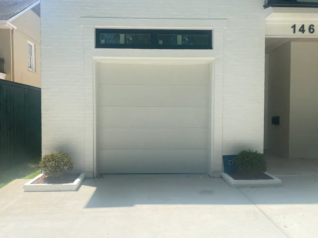White painted garage with rectangular window above the closed door, flanked by small potted plants.