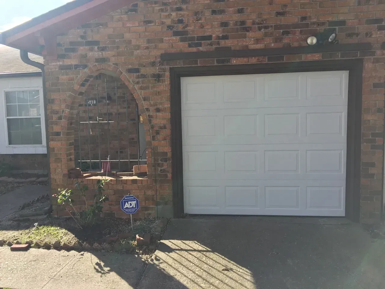 White garage door on brick house with an arched opening to the left.