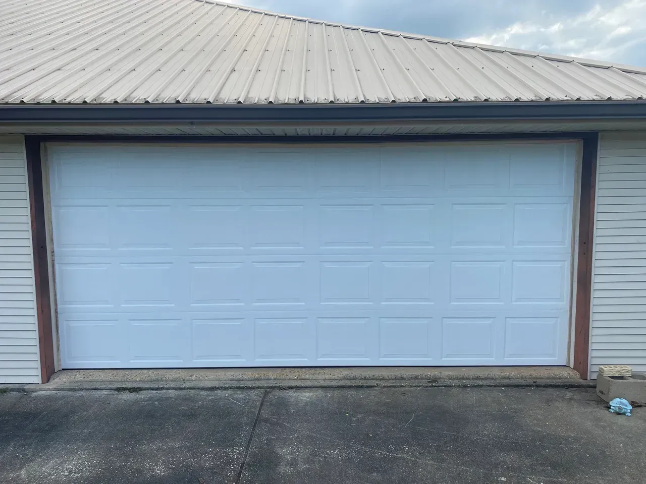 White garage door on a tan house with a metal roof. Concrete driveway in front.