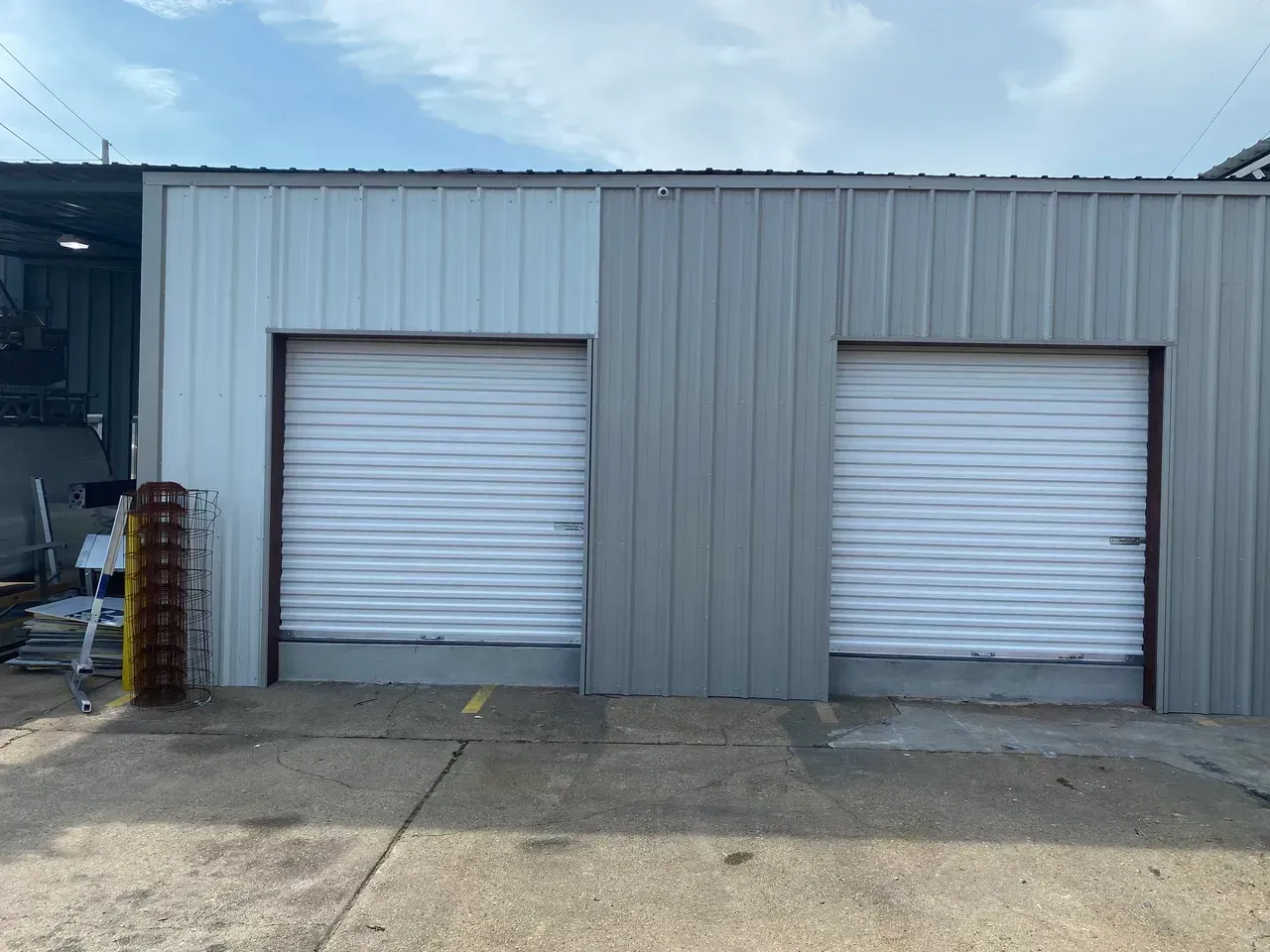 Metal building with two garage doors; one side painted light gray, the other dark gray.