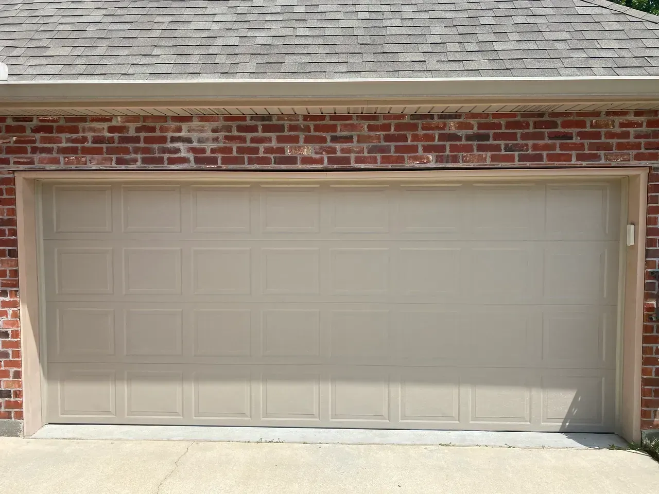Tan garage door with brick exterior and concrete driveway.