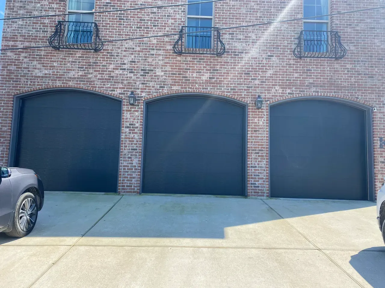 Three dark arched garage doors in brick building.