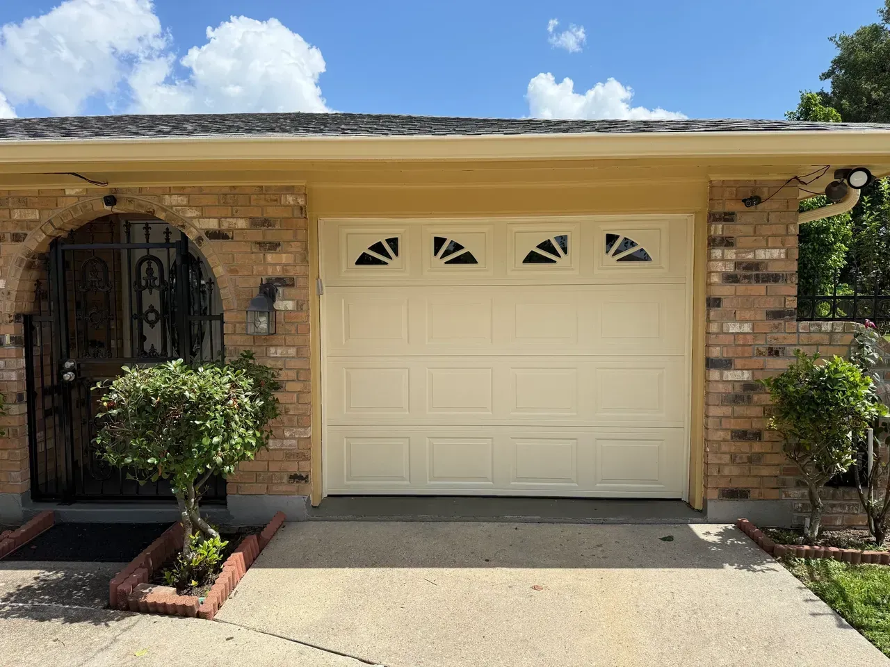 Beige garage door on a brick house with an arched entryway.