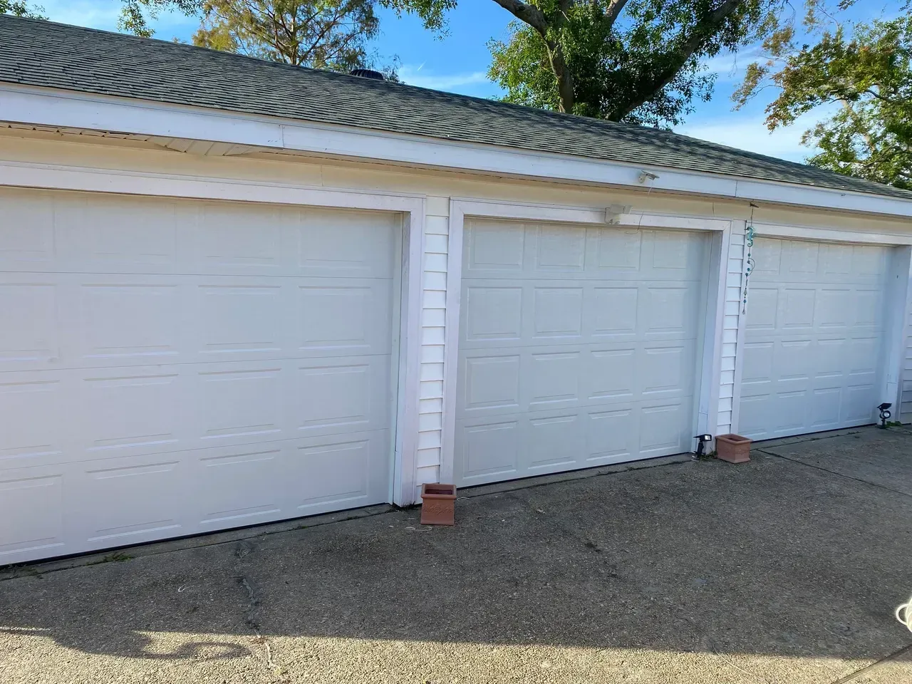 Three white garage doors with a grey roof and gravel driveway.
