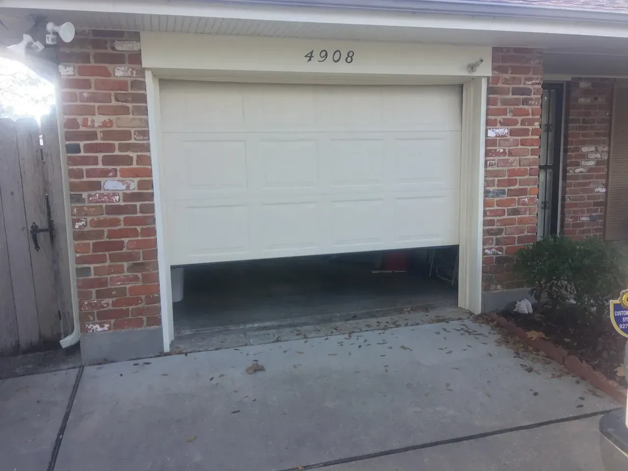 Partially open garage door on a brick house. Door is off track. Number 4908 above.
