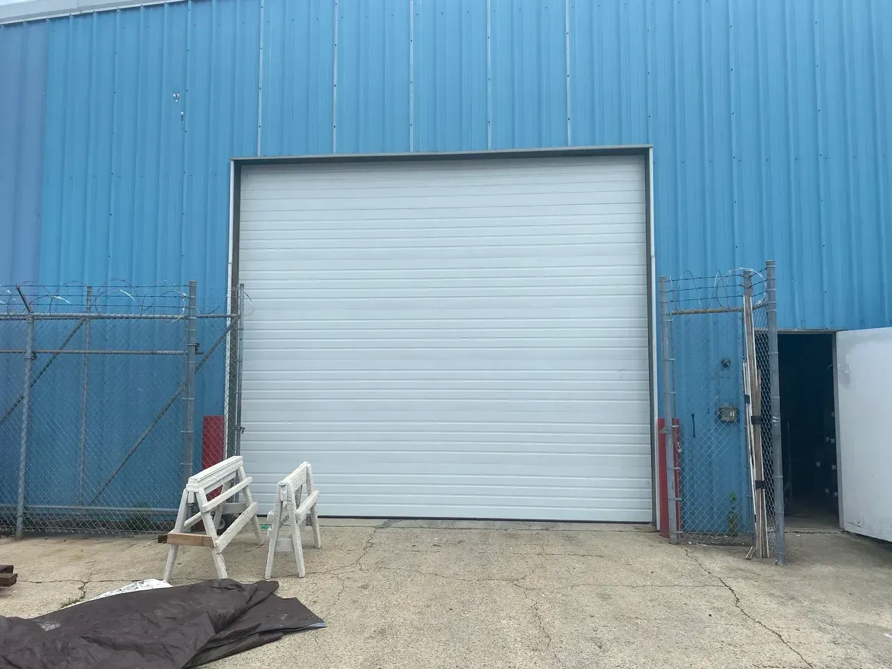 White garage door on blue building exterior, chain link fence, concrete.