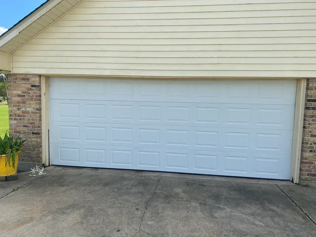 White garage door on a light tan house with brick accents, set on a cracked concrete driveway.