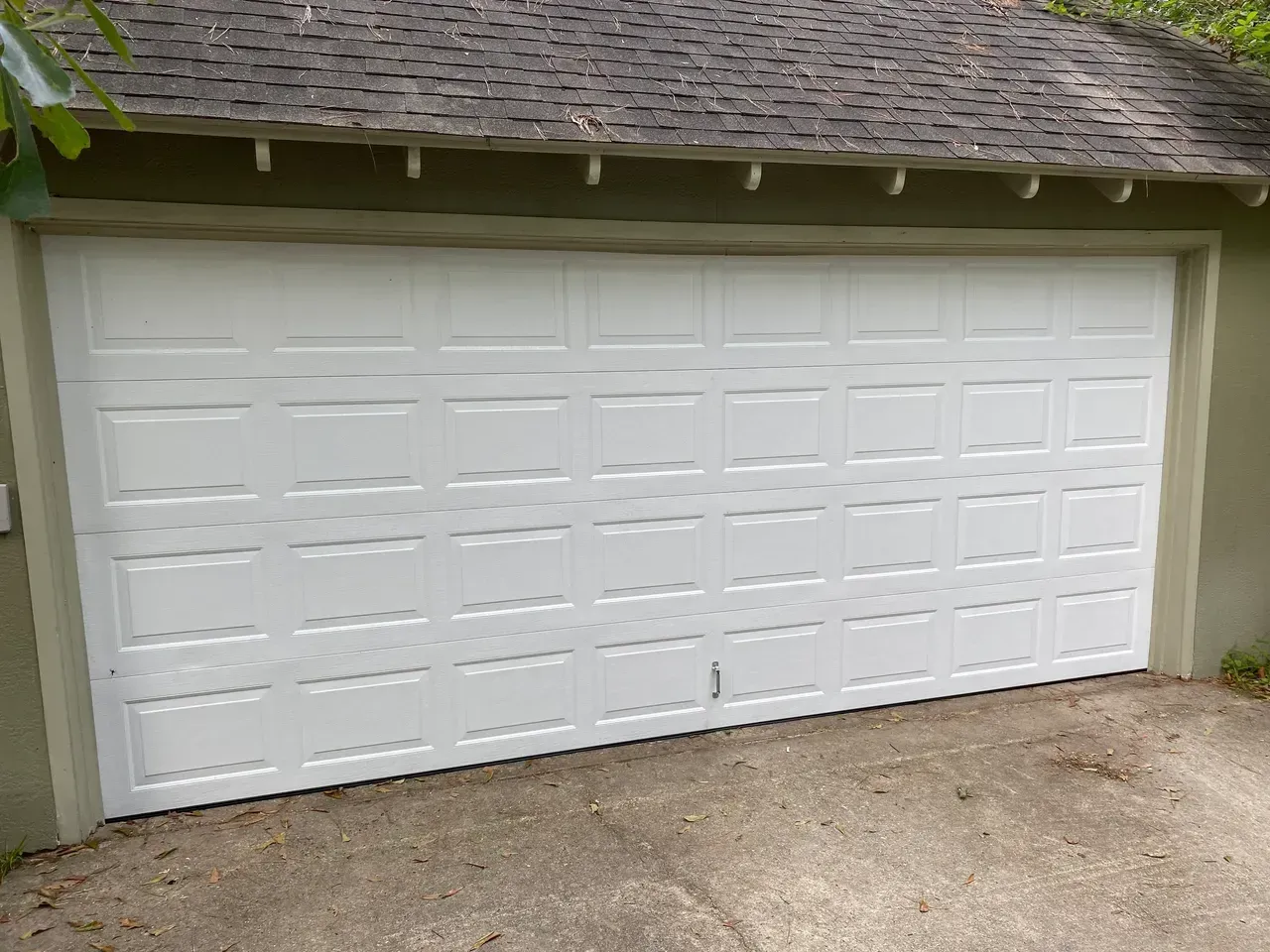White panel garage door on a tan building with a brown shingle roof.