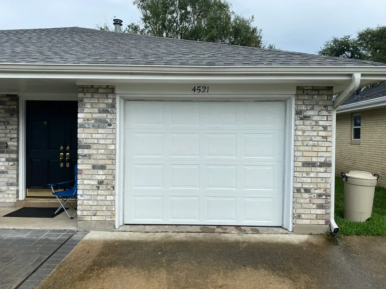 White garage door with brick facade, address 4521 above, dark blue door to the left, and a trash can to the right.