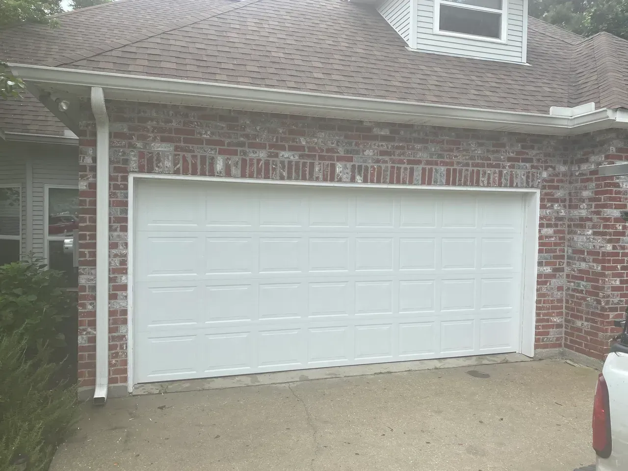 White garage door on a brick building with a brown roof.