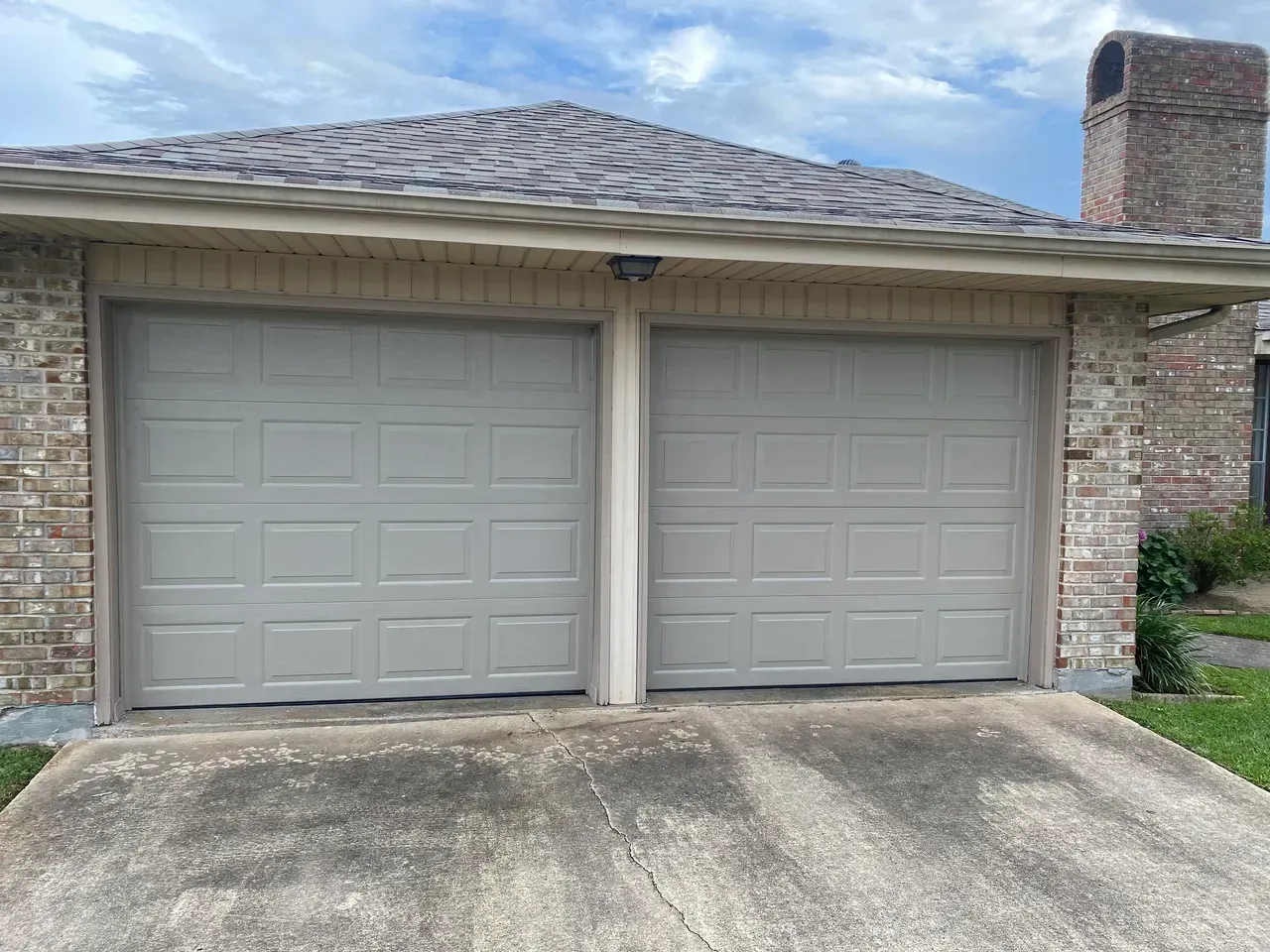 Two gray garage doors on a brick house with a concrete driveway and cloudy sky.