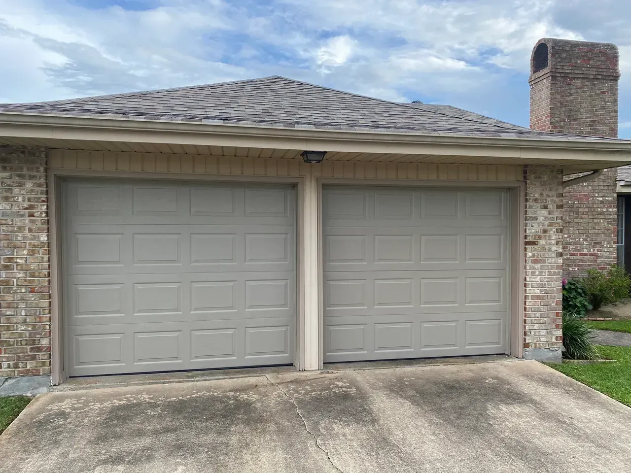 Two-car garage with gray doors, tan brick, and a chimney against a cloudy sky.