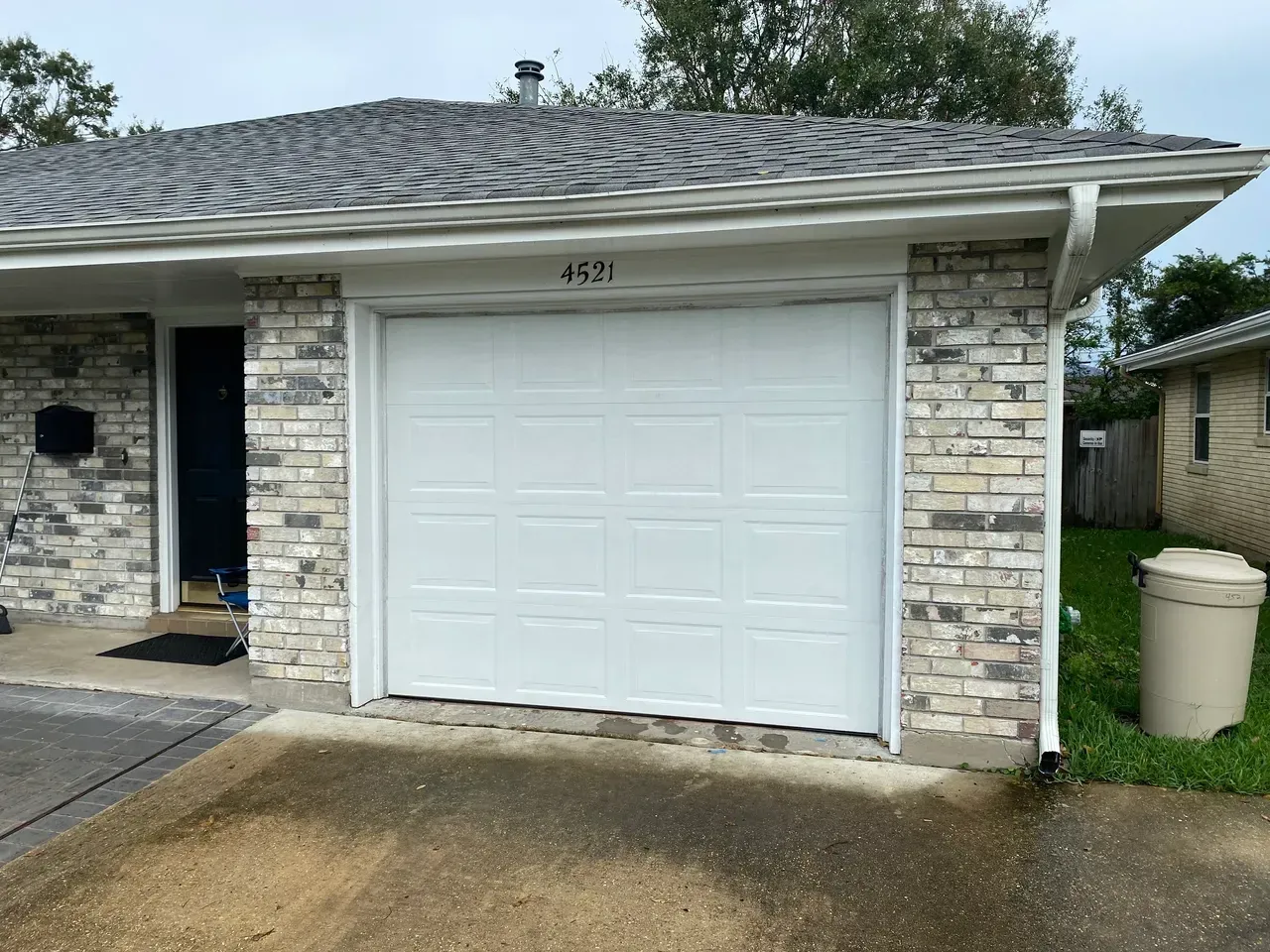 White garage door with gray brick facade. House number 