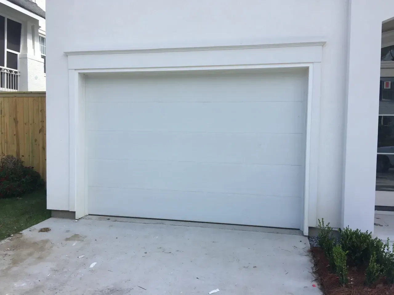 White garage door on a concrete driveway, framed by white molding.