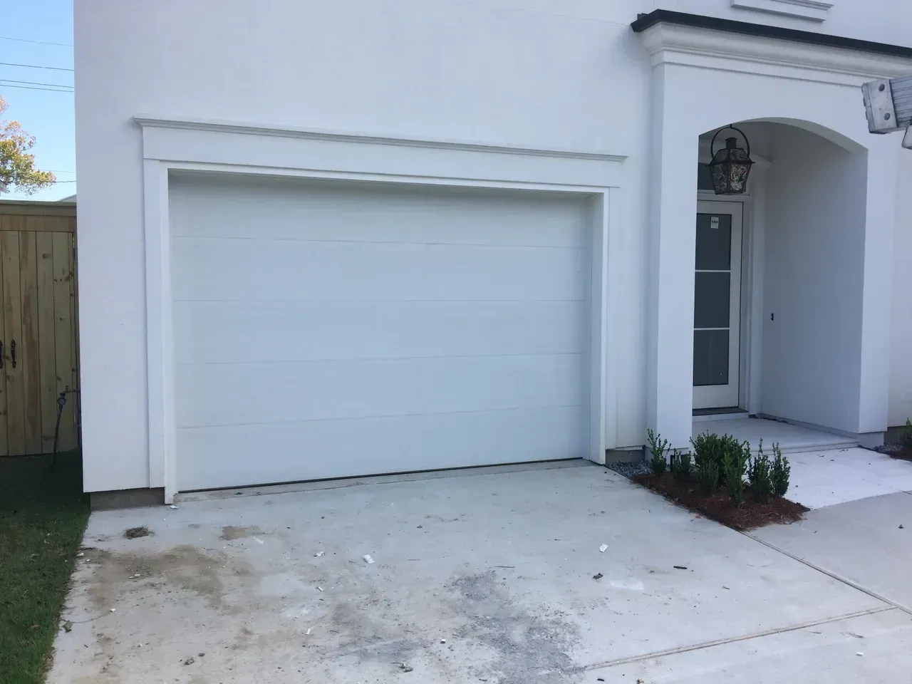 White garage door on a stucco house with a concrete driveway and small landscaping.