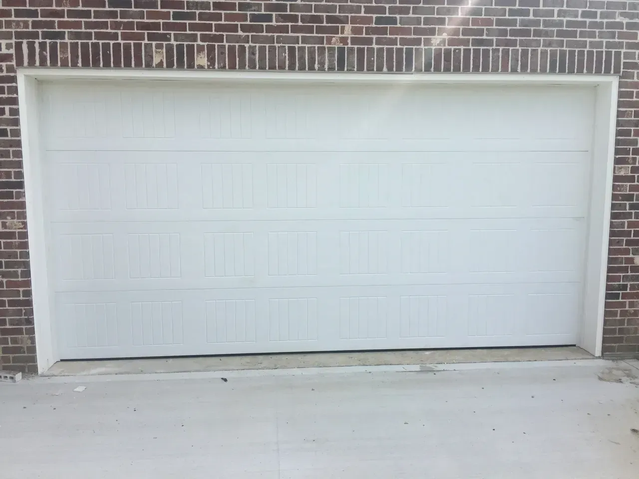 White garage door on a brick building with a concrete driveway.