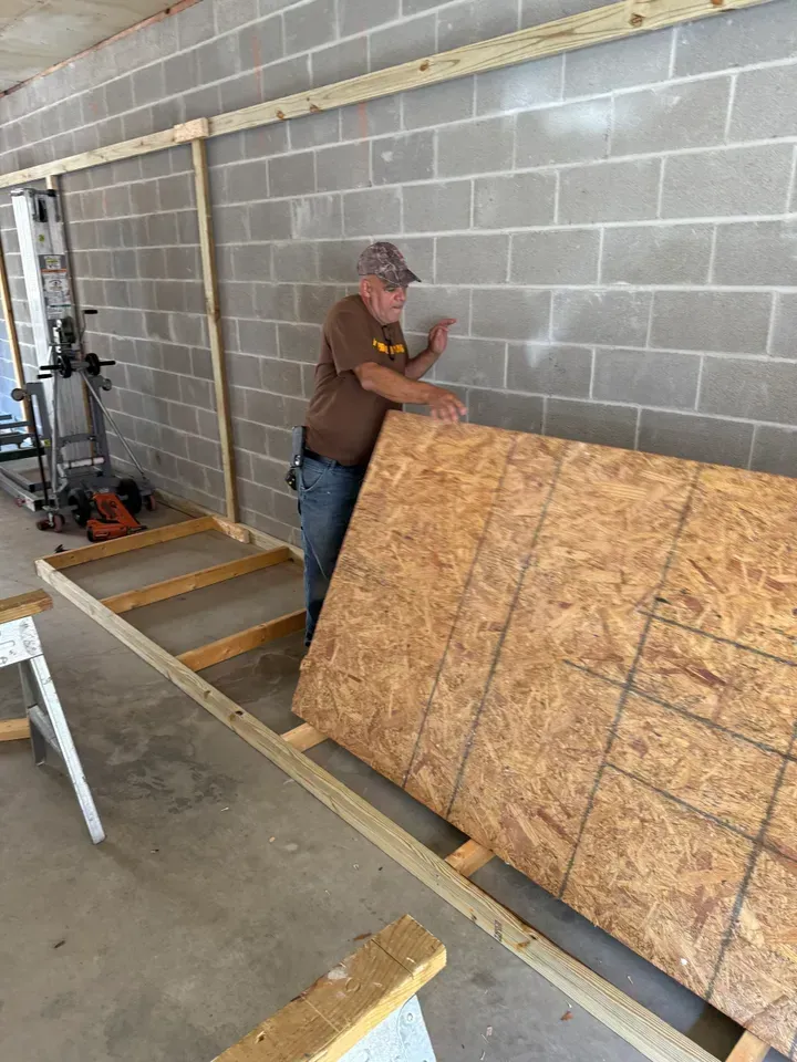 Man working on wood paneling on a cinder block wall, using a wood frame. Garage setting.