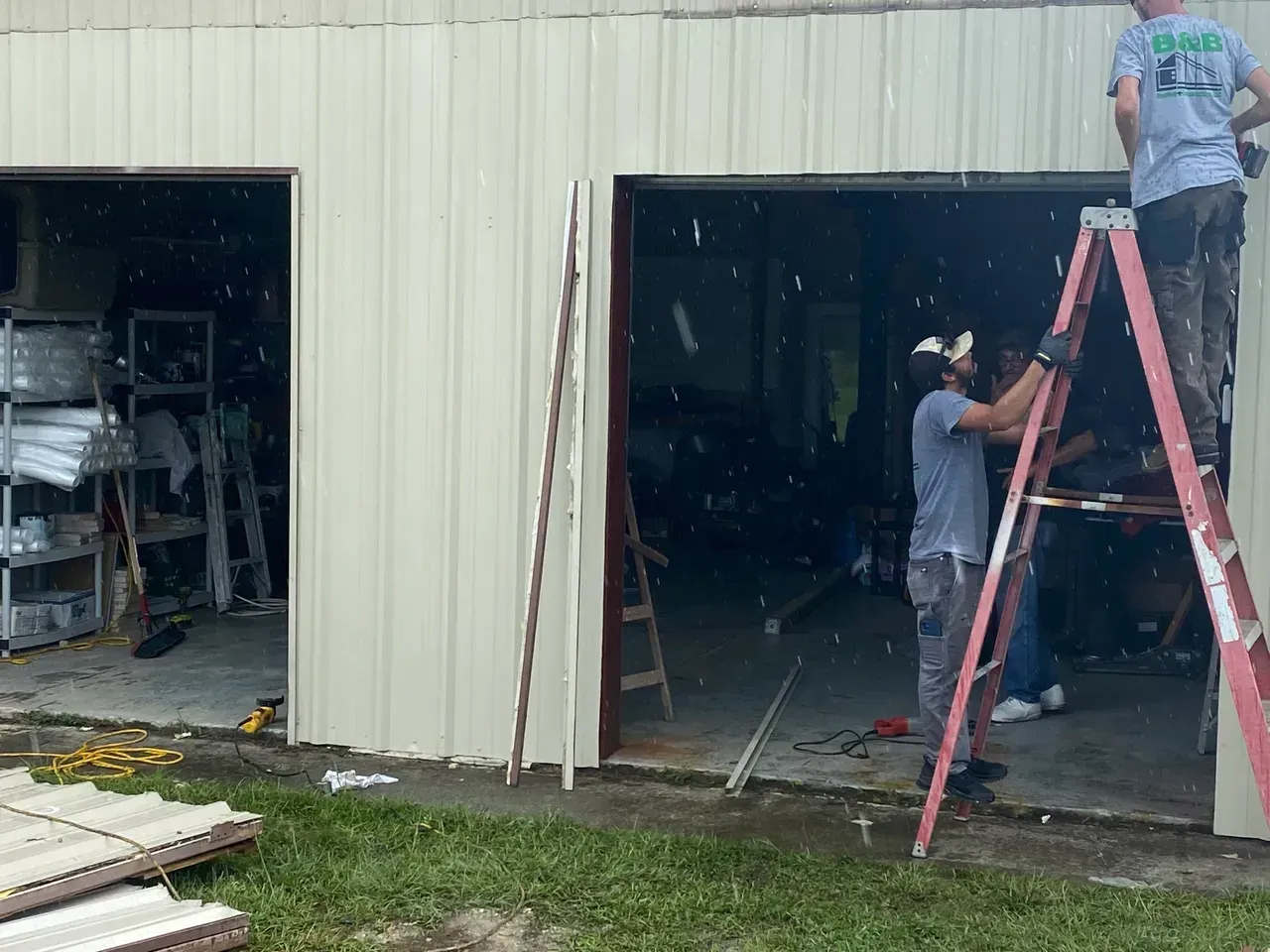 Workers installing trim around a garage door on a metal building, outdoors.