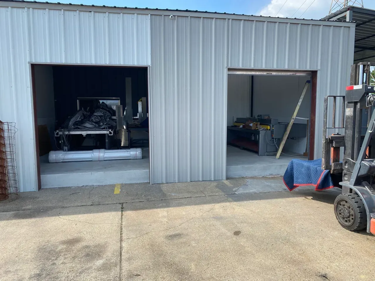 Metal building with two open garage doors; a forklift is parked near one.
