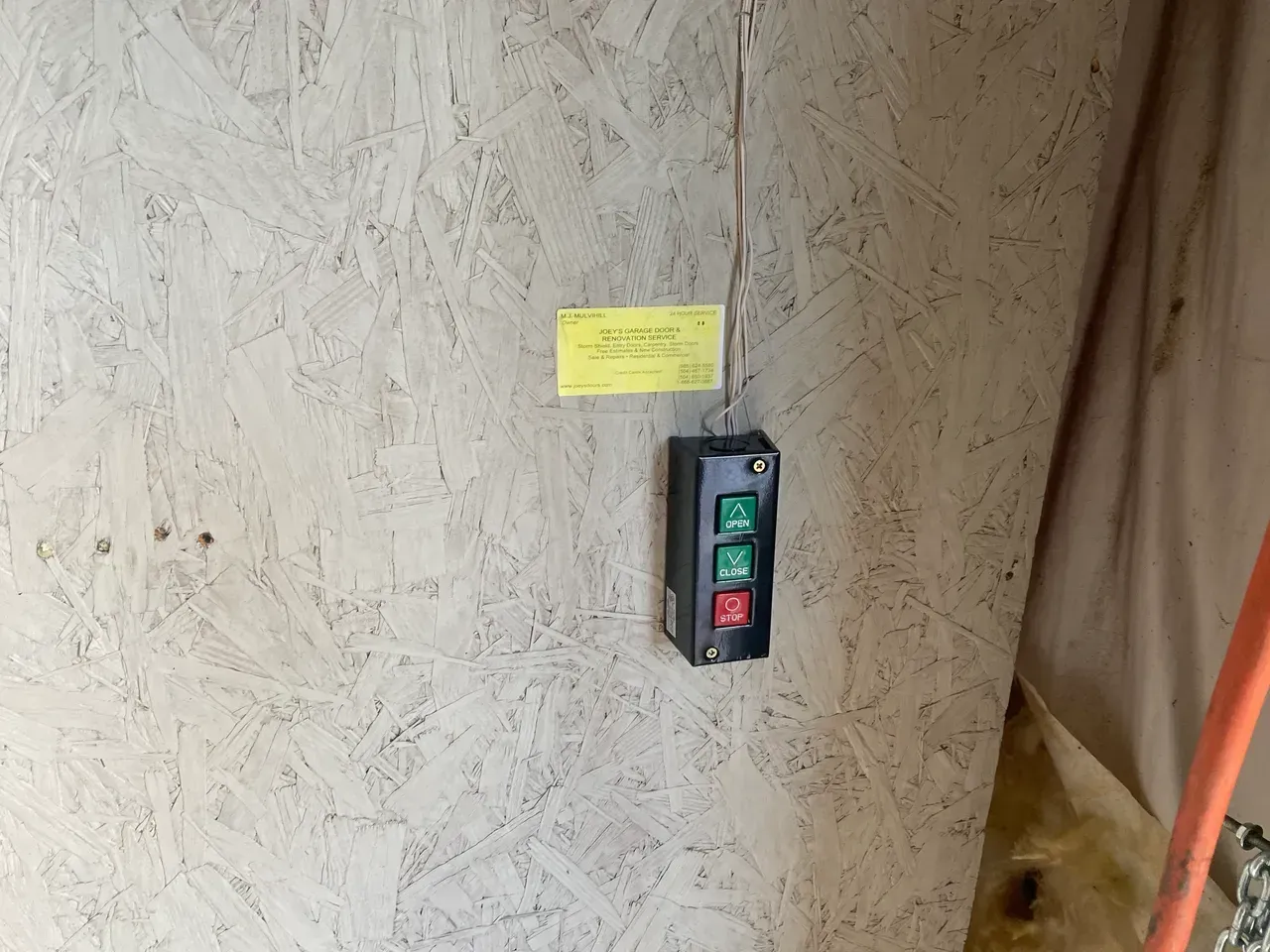 Black control box with green and red buttons mounted on a light wood wall.