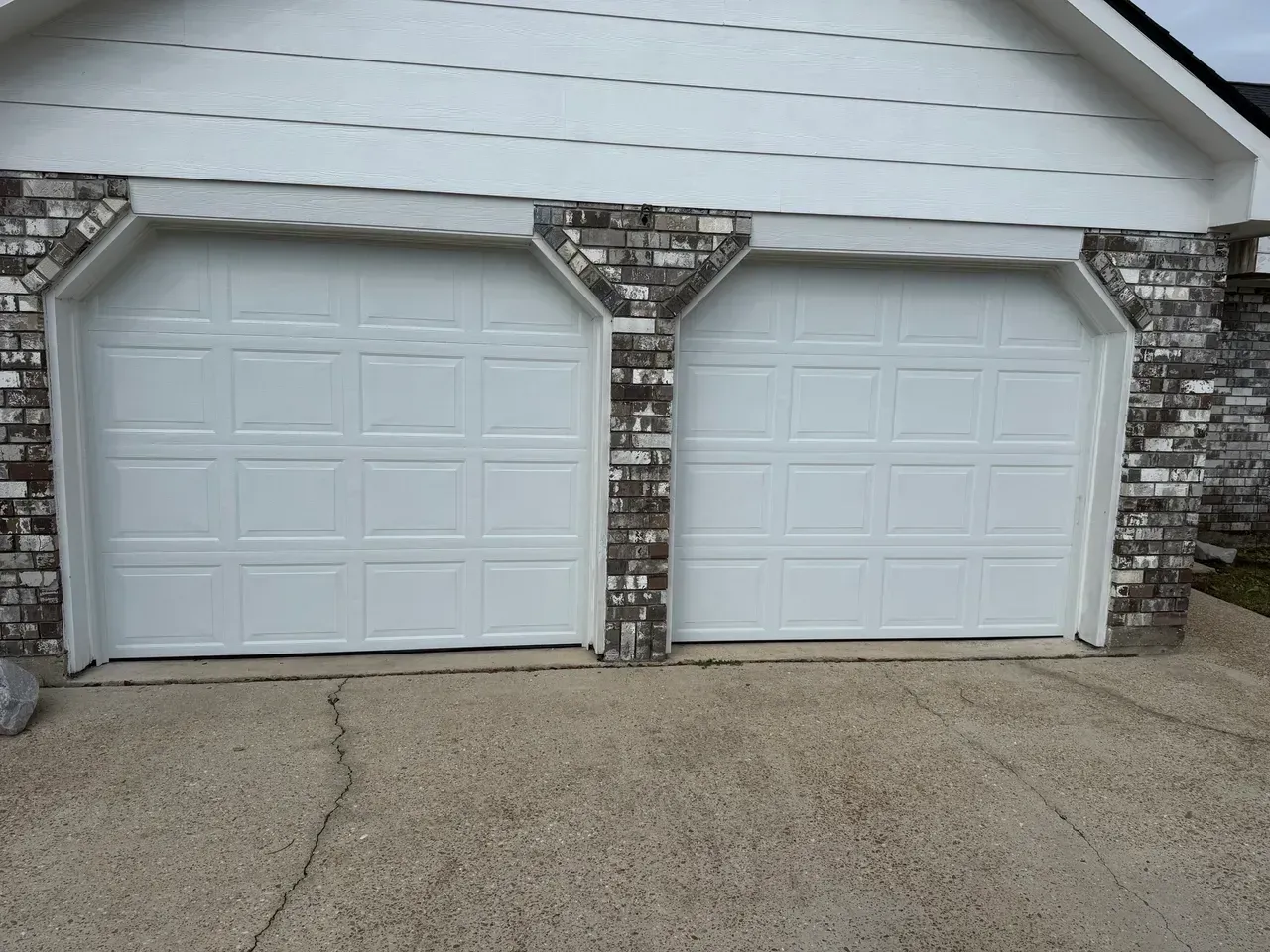 Two white garage doors with brick accents. Concrete driveway.