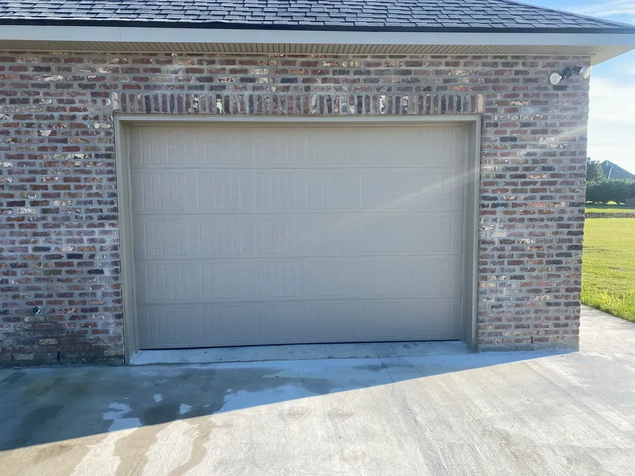 Tan garage door on a brick building with a concrete driveway.
