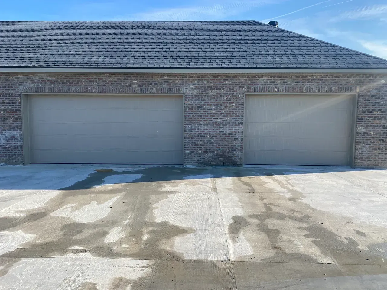 Two-car garage with tan doors and brick facade. Concrete driveway is wet.