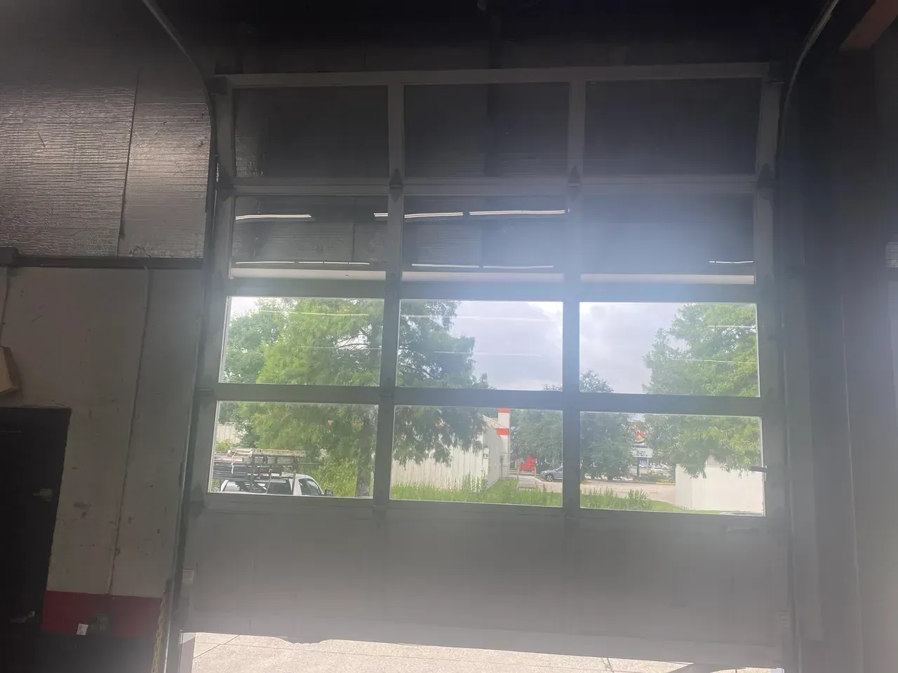 Garage door with glass panels open, showing trees and sky outside.