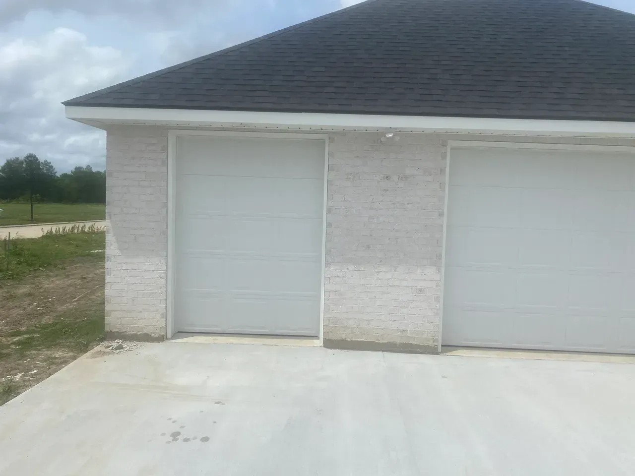 Garage with two white doors and a dark roof. Light-colored brick wall. Concrete driveway.