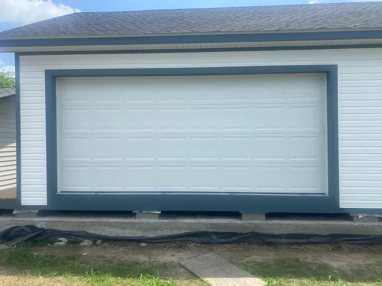 White garage door, trimmed in blue, on a white building with dark roof.