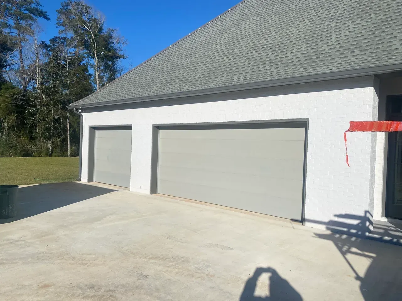 Two-car garage with gray doors, white stucco exterior, and gray roof. Concrete driveway in front.