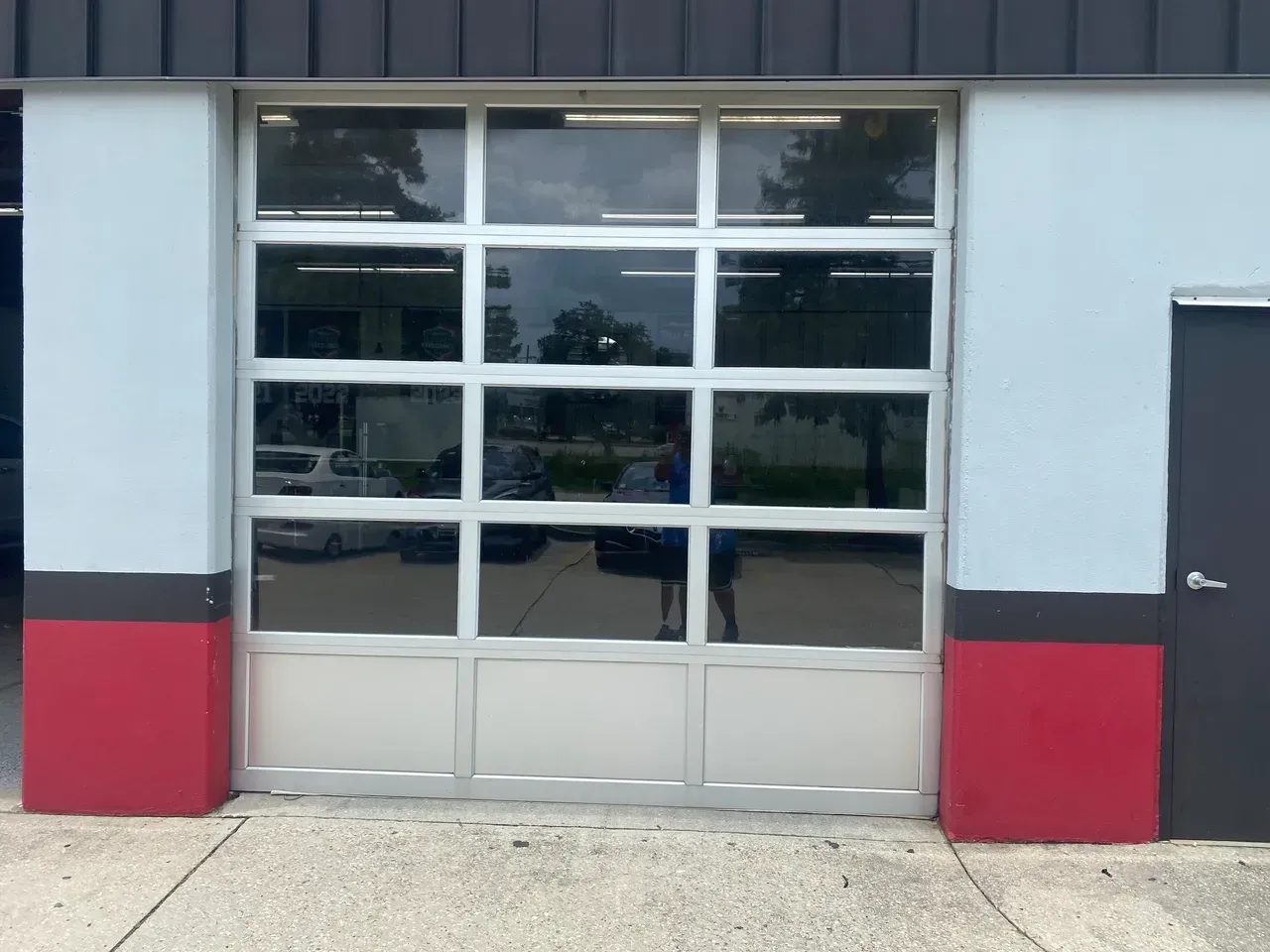 Glass garage door with a grid pattern, between red and blue walls, with a black door to the right.