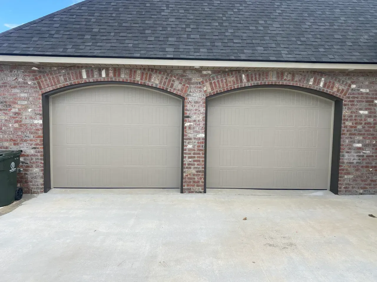 Two tan garage doors under brick arches on a brick building with a dark roof.