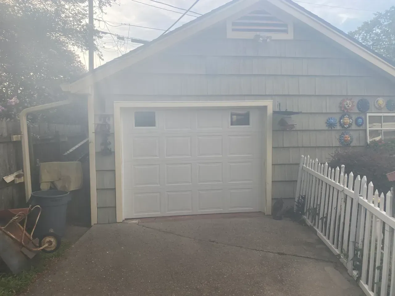 White garage door with windows, on a light blue-gray building. A white picket fence is on the right.